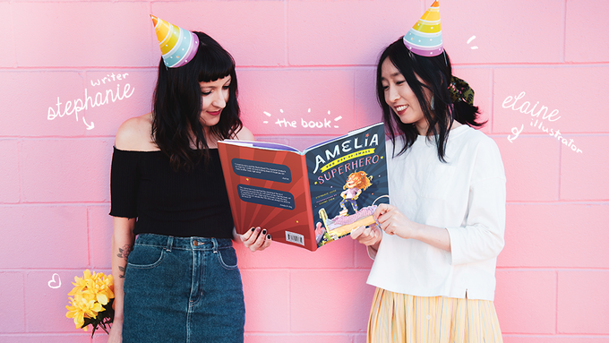 Vancouver author Stephanie Lecce and illustrator Elaine Chen standing in front of a pink wall and holding their children's book, Amelia the Not-So-Small Superhero